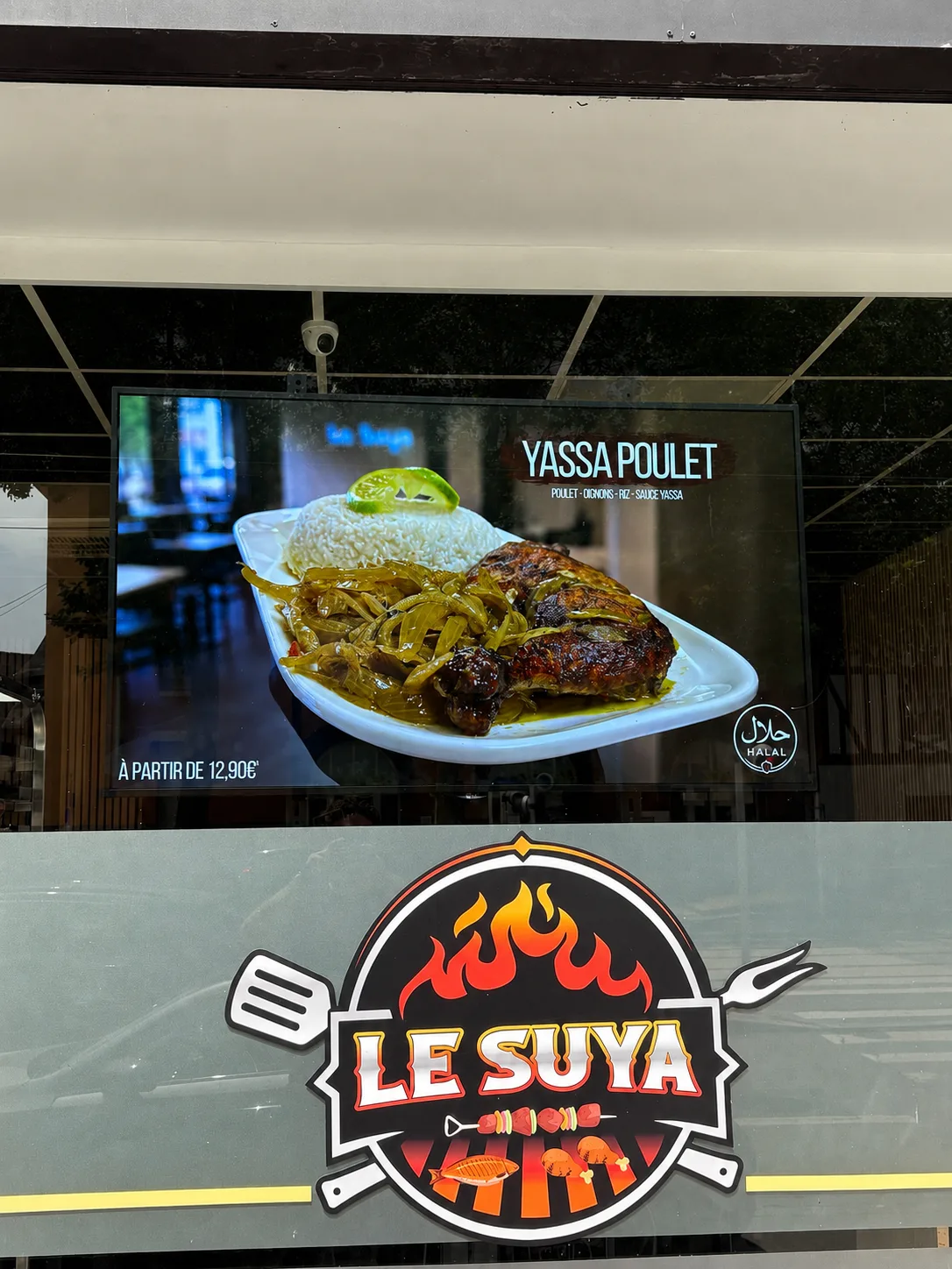 Écran en vitrine d'un restaurant affichant un plat en grand format derrière la vitre, au-dessus du logo de l'enseigne